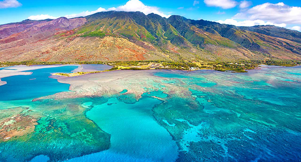 Vibrant turquoise waters meet a rugged mountain landscape under a bright sky.