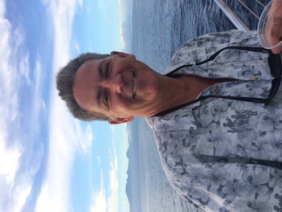 Man smiling on a boat with ocean and islands in the background.