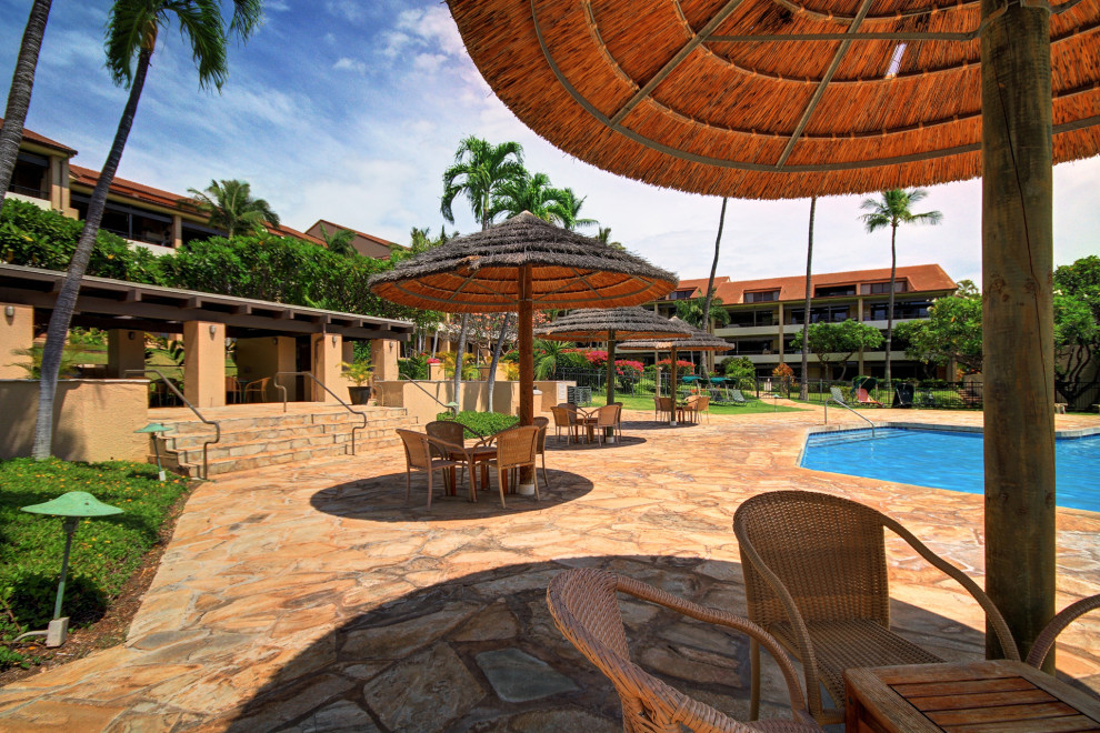 Sunny outdoor pool area with stone flooring and wicker furniture.
