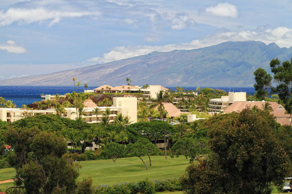 Scenic view of a golf course with buildings and mountains in the background.