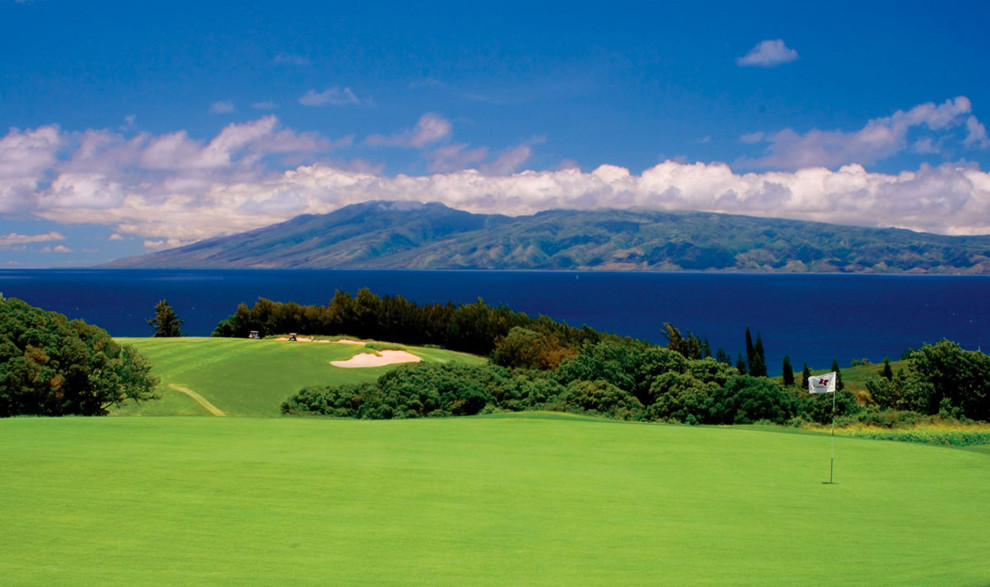 Scenic golf course overlooking a deep blue ocean and distant mountains.