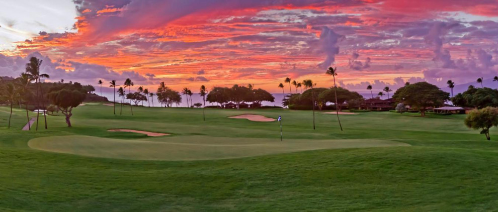 A golf course at sunset with vibrant orange and pink skies.